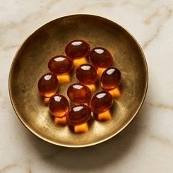 Amber softgels in a brass dish on marble